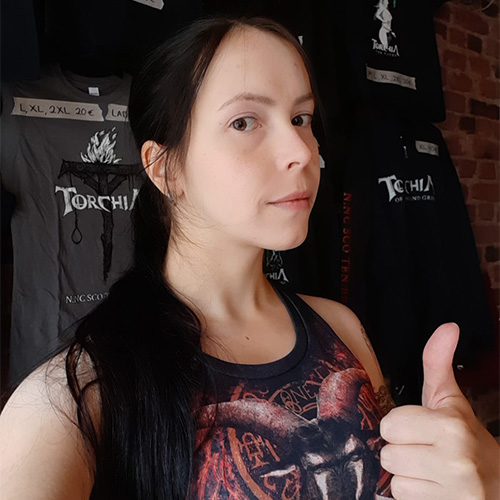 Photo of Janetta giving the camera a thumbsup while standing in front of Torchia t-shirts