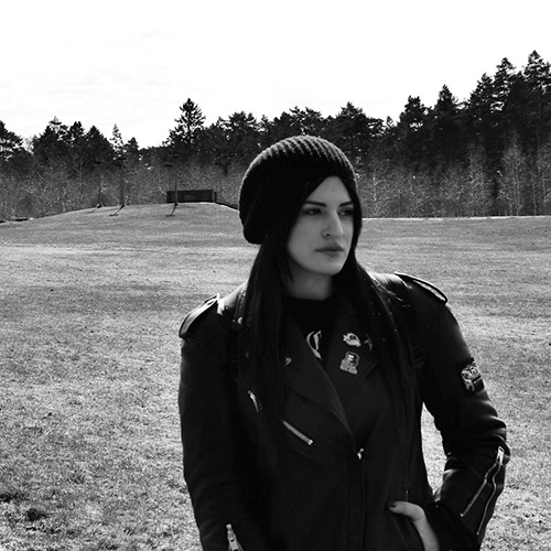 Artistic black and white portrait of Sofia standing in a field in front of a forest.